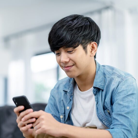 Happy,Asian,Teenager,Using,Smart,Phone,And,Smiling,On,Sofa
