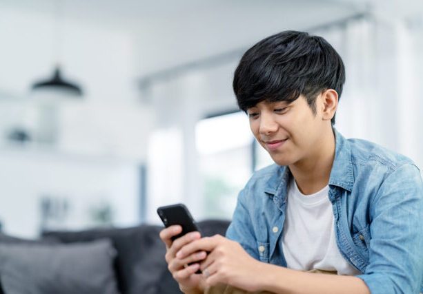 Happy,Asian,Teenager,Using,Smart,Phone,And,Smiling,On,Sofa