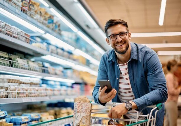 Happy,Man,Using,Smart,Phone,While,Shopping,In,Supermarket,And