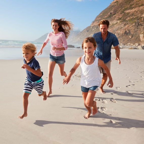 Parents,Running,Along,Beach,With,Children,On,Summer,Vacation